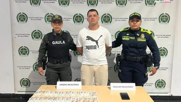 En la imagen está alias Chiki con dos servidoras de la Policía Nacional y adelante una mesa con un celular y dinero incautado