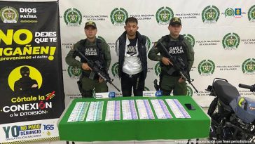 El capturado aparece detrás de una mesa en la que hay billetes de diferentes denominaciones. Dos personas del Gaula rodean al capturado. Al fondo se ve un banner de la Policía.