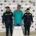 En la imagen se ve una persona detenida bajo custodia de dos integrantes de la Policía Nacional.