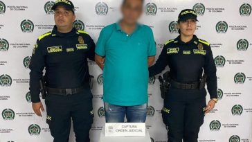 En la imagen se ve una persona detenida bajo custodia de dos integrantes de la Policía Nacional.