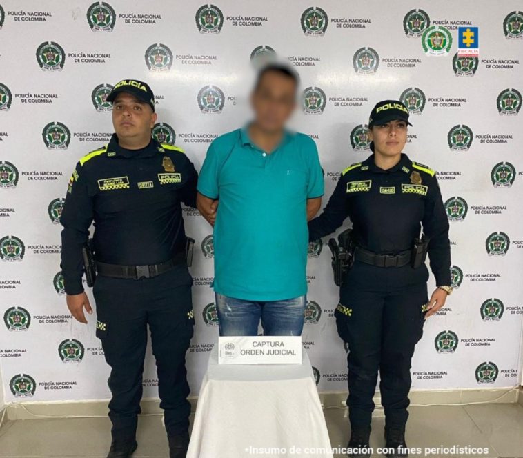 En la imagen se ve una persona detenida bajo custodia de dos integrantes de la Policía Nacional.