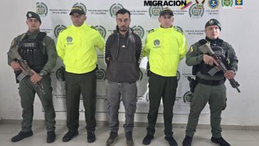 En la foto se observan cinco personas, una de ellas es el capturado y cuatro uniformados de la Policía Nacional. En la parte posterior un backing de la Polcía Nacional.