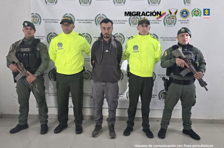 En la foto se observan cinco personas, una de ellas es el capturado y cuatro uniformados de la Policía Nacional. En la parte posterior un backing de la Polcía Nacional.