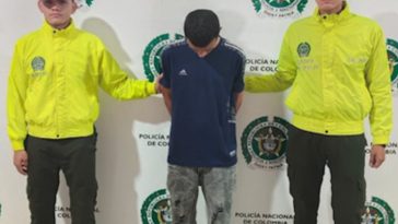 en la imagen se ve una persona detenida bajo custodia de dos integrantes de la policía Nacional.