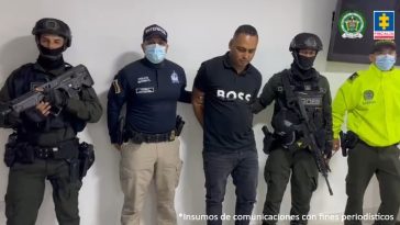 El capturado aparece en medio de la imagen, rodeado de personal de Goes, Policía e Interpol. Está esposado con las manos atrás.