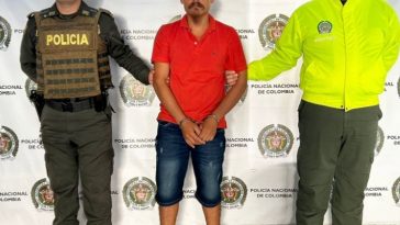 en la imagen se ve una persona detenida bajo custodia de dos integrantes de la Policía Nacional.