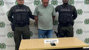 En la foto está el procesado con dos servidores del Gaula de la Policía a los lados y al fondo un pendón con múltiples logos de la Policía. 