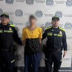 En la imagen se ve un hombre detenido bajo custodia de integrantes de la Policía Nacional