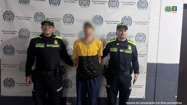 En la imagen se ve un hombre detenido bajo custodia de integrantes de la Policía Nacional