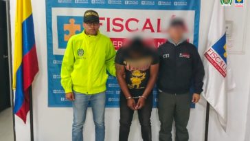 En la fotografía aparece el capturado junto a un funcionario del CTI y un integrante de la Policía Nacional. En la parte superior está un banner de la Fiscalía General.