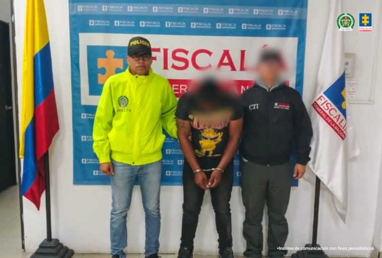 En la fotografía aparece el capturado junto a un funcionario del CTI y un integrante de la Policía Nacional. En la parte superior está un banner de la Fiscalía General.