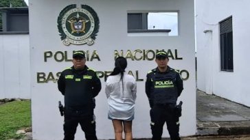 La mujer capturada aparece de espaldas, con dos miembros de la Policía a su lado. Al fondo puede leerse "Policía Nacional".