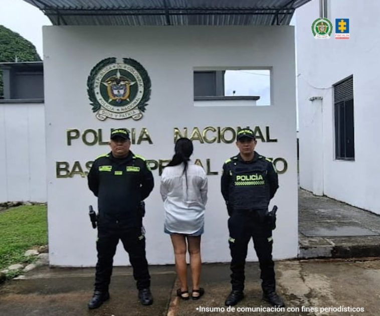 La mujer capturada aparece de espaldas, con dos miembros de la Policía a su lado. Al fondo puede leerse "Policía Nacional".