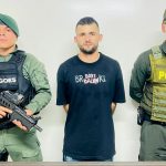 En la fotografía se aprecia de pie y con los brazos atrás a Jhon Fredy Ramírez Bedoya, alias Barbado. Usa barba y viste camiseta de manga corta de color negro, con estampado a la altura del pecho. A sus extremos hay personal de la Policía Nacional. Delante de ellos hay una superficie y sobre ella hay un letrero que dice: ‘Captura por orden judicial’.