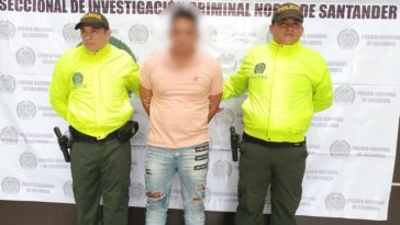 Se visualiza al capturado junto a dos uniformados de la Policía Nacional. Detrás el banner institucional que identifica a la Dirección de Investigación de la Policía Nacional en Norte de Santander 