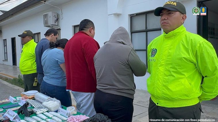 Los cuatro capturados aparecen de espaldas. Los rodean dos miembros de la Policía. Frente a ellos aparecen varios estupefacientes incautados.