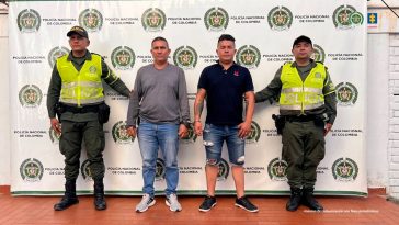 Los capturados se encuentran de frente y  custodiados por dos uniformados de la Policía Nacional. En la foto se ve de fondo un backing de la Policía Nacional.