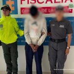 El capturado aparece esposado, en medio de una servidora de la Fiscalía y una de la Policía. Al fondo se ve un banner de la Fiscalía