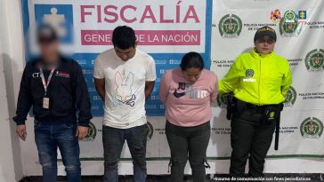 Los capturados se encuentran de frente y custodiados por un servidor del Cuerpo Técnico de Investigación CTI y un uniformado de la Sijin de la Policía Nacional. En la foto se ve de fondo un backing de la Fiscalía y Policía.