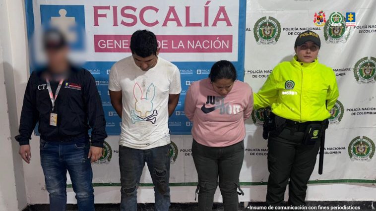 Los capturados se encuentran de frente y custodiados por un servidor del Cuerpo Técnico de Investigación CTI y un uniformado de la Sijin de la Policía Nacional. En la foto se ve de fondo un backing de la Fiscalía y Policía.