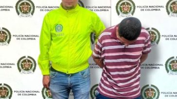 en la imagen se ve una persona detenida bajo custodia de un integrante de la Policía Nacional. Detrás suyo un backing institucional.