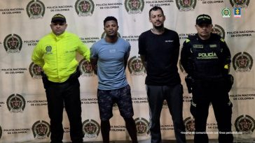 En la fotografía se observan cuatro personas, dos de ellas los capturados y dos uniformados de la Policía en la parte posterior un backing con escudos de la Policía Nacional.