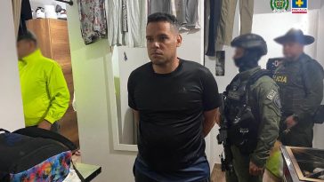 El hombre se ve en el centro de la imagen, dentro de una vivienda. Al fondo puede verse ropa colgada y une spejo, además de miembros del Goes y la Policía. Está esposado, con las manos atrás.