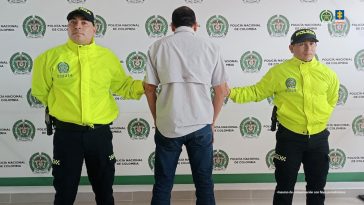 El capturado aparece de espalda a la cámara y está custodiado por dos uniformados de la policía nacional.