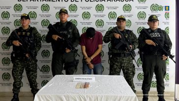 Se visualiza al capturado junto a uniformados del Gaula del Ejército y Policía Nacional. Frente a ellos una mesa con el dinero incautado al momento de la captura. Detrás el banner de la Policía Nacional.