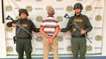 Se observa al capturado de espaldas junto a dos uniformados de la Policía Nacional. Detrás de ellos el banner que identifica a la Policía Nacional.