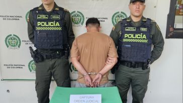 En la imagen se ve una persona detenida de espaldas, bajo custodia de dos integrantes de la Policía Nacional.