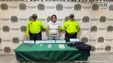 En la imagen está la procesada con dos servidores de la Policía Nacional y adelante una mesa con celulares, 4 cédulas de ciudadanía, 1 frasco de gotas  y una tableta de pastillas de clonazapam y varios elementos de propiedad de la víctma.