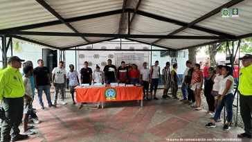 capturados de frente custodiados por policías, delante de ellos mesa con material incautado, detrás banner de la Policía Nacional.