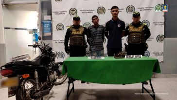 En la fotografía se observan cuatro personas, dos de ellas los procesados y dos uniformados de la Policía Nacional. En la parte posterior un backing con escudos de la Policía. 