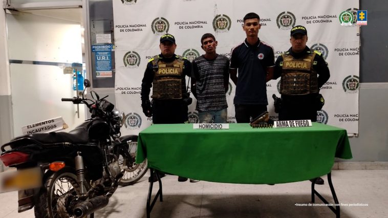 En la fotografía se observan cuatro personas, dos de ellas los procesados y dos uniformados de la Policía Nacional. En la parte posterior un backing con escudos de la Policía. 