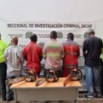 En la imagen se ve a cinco hombres de espalda en compañía de dos uniformados de la Policía Nacional, quienes serían los presuntos responsables de generar carbón vegetal en un área de protección ambiental en Cali. Estas personas fueron capturadas en una acción conjunta con la Dirección de Carabineros.