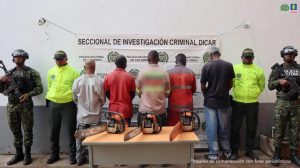 En la imagen se ve a cinco hombres de espalda en compañía de dos uniformados de la Policía Nacional, quienes serían los presuntos responsables de generar carbón vegetal en un área de protección ambiental en Cali. Estas personas fueron capturadas en una acción conjunta con la Dirección de Carabineros.