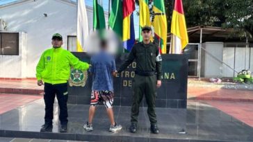 El capturado se encuentra de espaldas y en custodia por dos uniformados de la Policía Nacional.