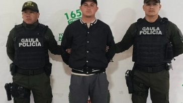 El capturado se encuentra de frente y custodiado por dos uniformados del Gaula de la Policía Nacional. En la foto se ve de fondo un backing de la Policía.