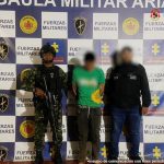 capturado de frente custodiado por investigador del CTI de la Fiscalía y un soldado. Detrás banner del grupo Gaula Militar.