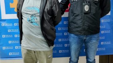 Óscar Arbey Yarce Berrio está en la foto acompañado por un funcionario del CTI de la Fiscalía y en la parte de atrás se ve backing con los logos de la Fiscalía.